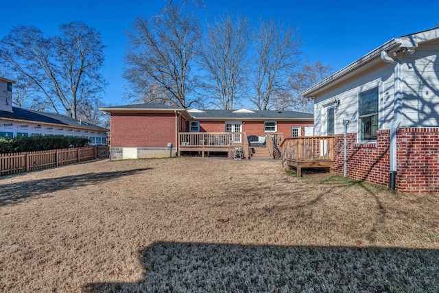 back of property with a yard, fence, a deck, and brick siding