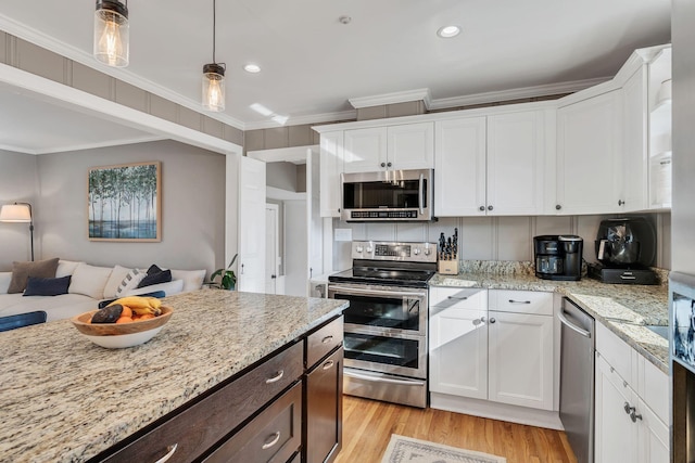 kitchen with appliances with stainless steel finishes, open floor plan, white cabinetry, and ornamental molding