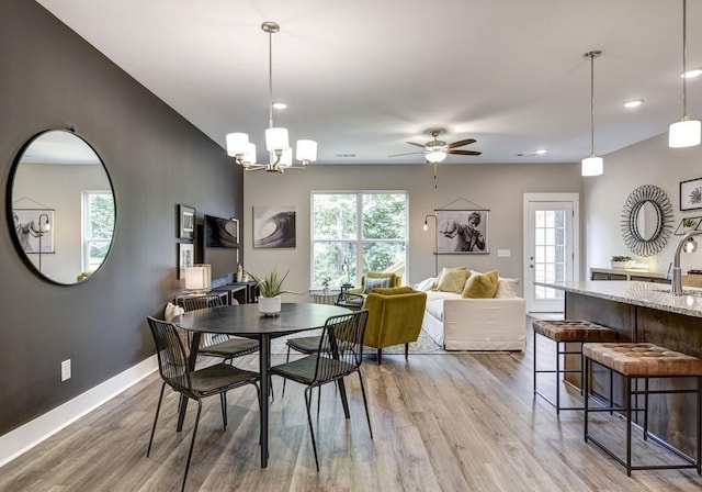 dining area with sink, ceiling fan with notable chandelier, and light wood-type flooring