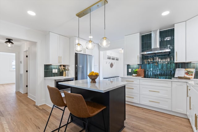 kitchen with a center island, backsplash, wall chimney exhaust hood, white cabinetry, and stainless steel refrigerator