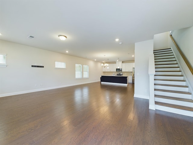 unfurnished living room featuring dark wood-type flooring and a notable chandelier