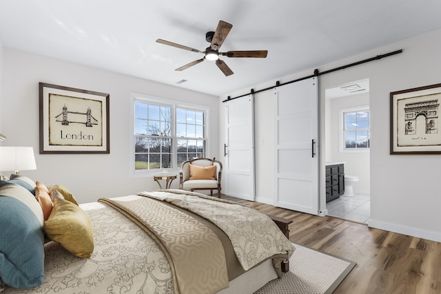 bedroom with ceiling fan, a barn door, hardwood / wood-style flooring, and ensuite bath