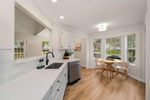 kitchen featuring decorative backsplash, stainless steel dishwasher, sink, white cabinets, and light hardwood / wood-style floors