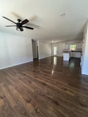 unfurnished living room featuring ceiling fan and dark wood-type flooring