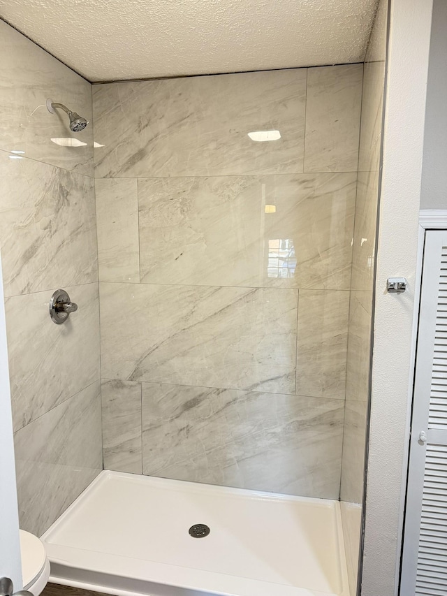 bathroom with tiled shower, a textured ceiling, and toilet