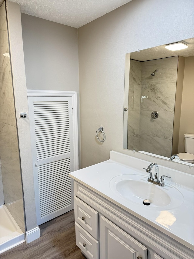 bathroom with walk in shower, vanity, a textured ceiling, hardwood / wood-style flooring, and toilet