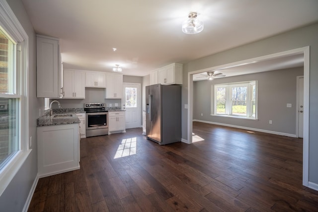 kitchen with appliances with stainless steel finishes, dark stone counters, a healthy amount of sunlight, sink, and white cabinetry