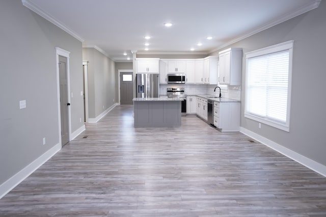 kitchen featuring a center island, light stone counters, backsplash, crown molding, and appliances with stainless steel finishes