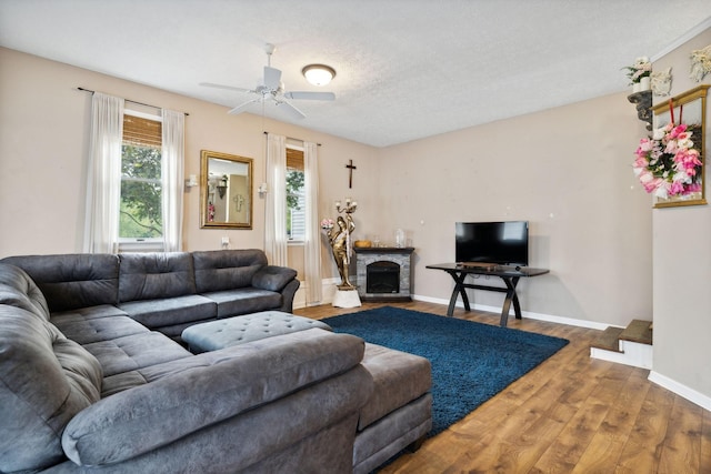 living room with ceiling fan, a fireplace, hardwood / wood-style floors, and a textured ceiling