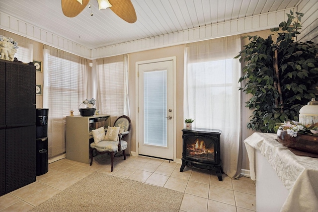 interior space featuring light tile patterned floors, a wood stove, and ceiling fan