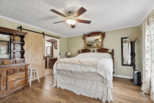 bedroom featuring ceiling fan, a barn door, a textured ceiling, hardwood / wood-style flooring, and ornamental molding