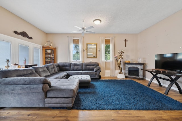 living room with a stone fireplace, ceiling fan, hardwood / wood-style floors, and a textured ceiling