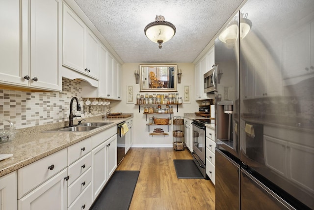 kitchen featuring sink, light stone counters, light hardwood / wood-style floors, white cabinets, and appliances with stainless steel finishes