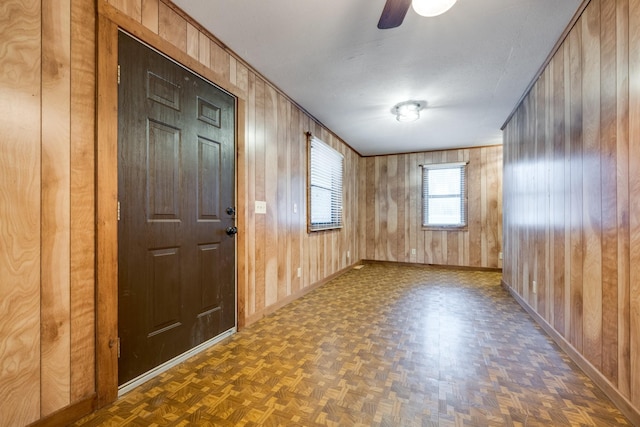 entryway featuring dark parquet floors, ceiling fan, ornamental molding, and wood walls