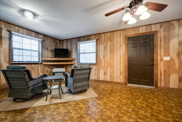 living area featuring wooden walls, parquet floors, a textured ceiling, and ceiling fan