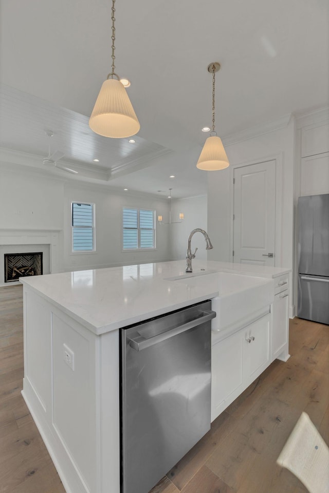 kitchen with a sink, light wood-style floors, white cabinets, appliances with stainless steel finishes, and an island with sink