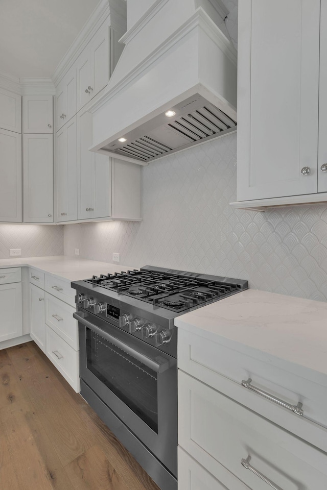 kitchen featuring premium range hood, white cabinetry, backsplash, stainless steel range with gas cooktop, and dark wood finished floors