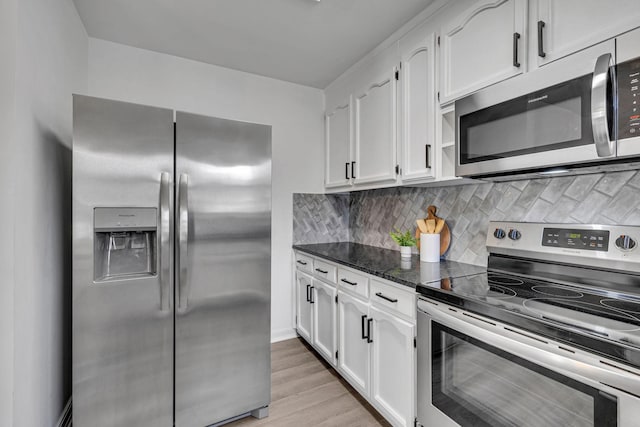 kitchen with tasteful backsplash, dark stone counters, stainless steel appliances, light hardwood / wood-style flooring, and white cabinets