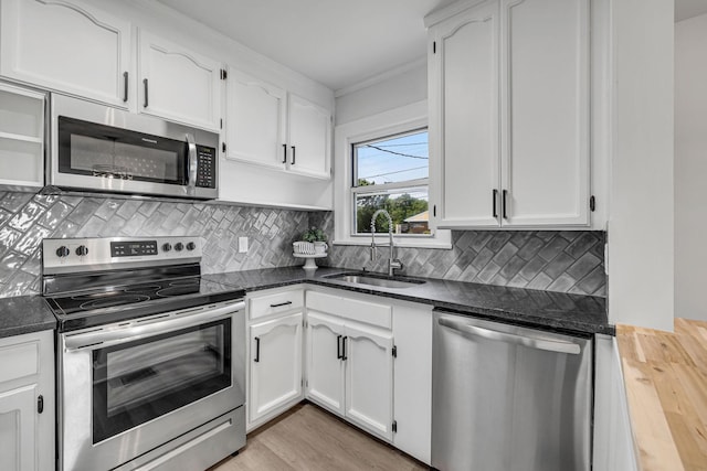 kitchen with sink, light hardwood / wood-style flooring, dark stone countertops, white cabinetry, and stainless steel appliances