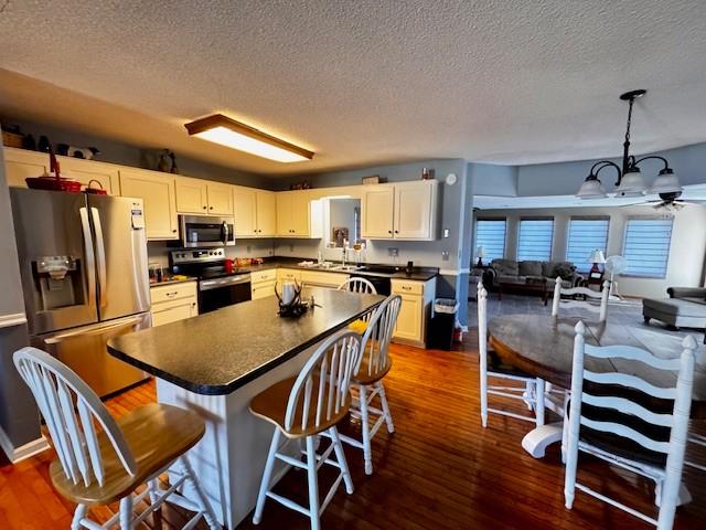 kitchen featuring a kitchen bar, stainless steel appliances, ceiling fan, dark wood-type flooring, and hanging light fixtures