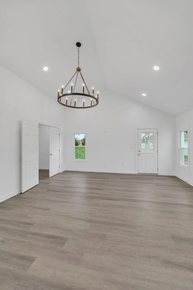 spare room featuring a chandelier, lofted ceiling, a wealth of natural light, and light hardwood / wood-style flooring