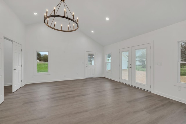 unfurnished living room featuring light hardwood / wood-style floors, french doors, high vaulted ceiling, and a chandelier