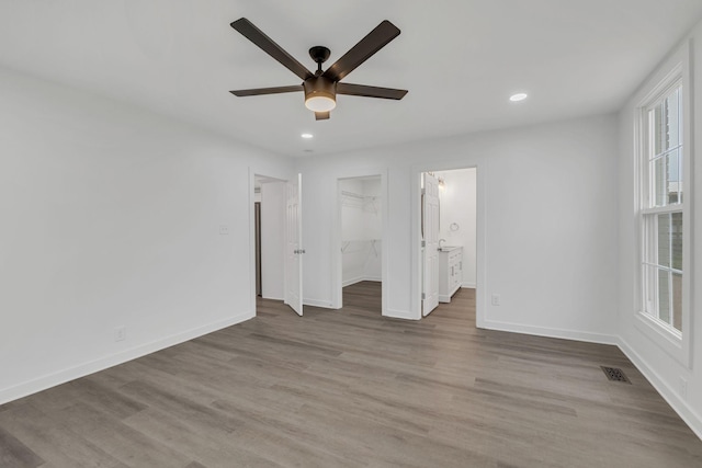 unfurnished bedroom with ceiling fan, a spacious closet, light hardwood / wood-style flooring, connected bathroom, and a closet