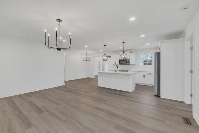 kitchen featuring hanging light fixtures, appliances with stainless steel finishes, a center island with sink, white cabinets, and light wood-type flooring