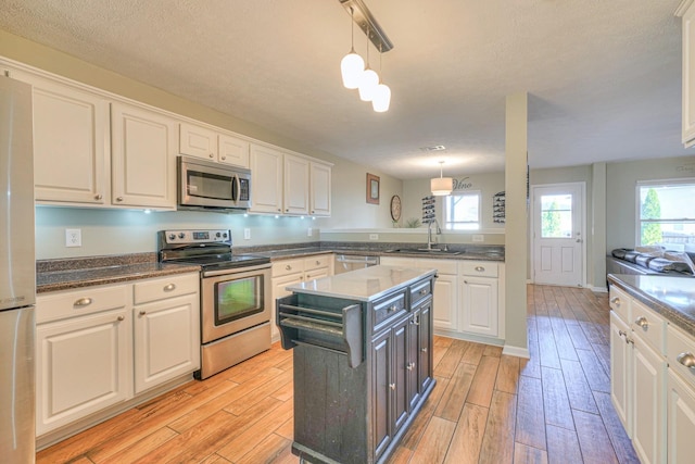 kitchen with a center island, white cabinets, sink, appliances with stainless steel finishes, and decorative light fixtures