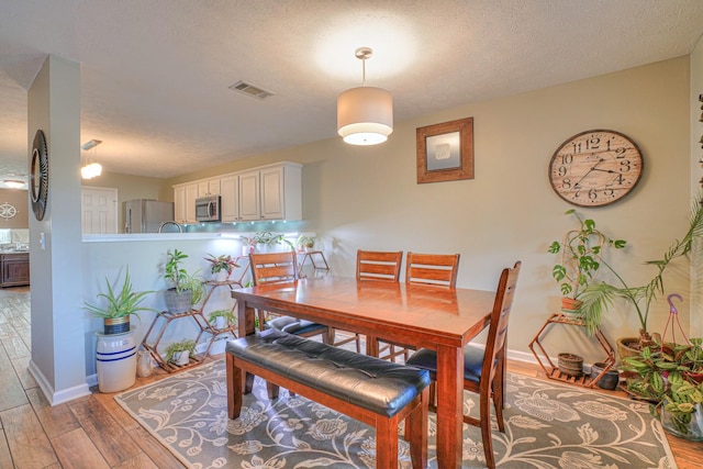 dining space with light wood-type flooring and a textured ceiling