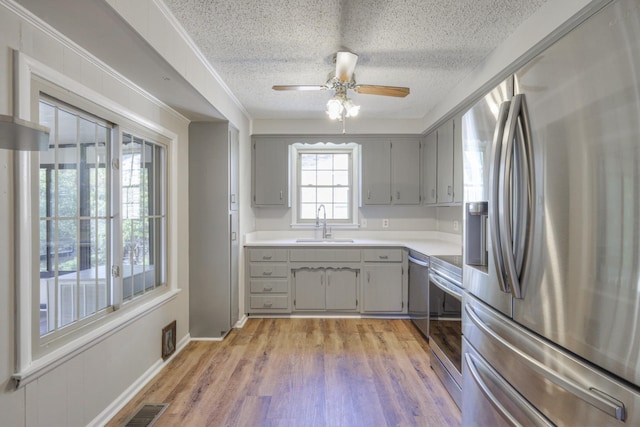 kitchen with gray cabinetry, a sink, visible vents, light wood-style floors, and appliances with stainless steel finishes