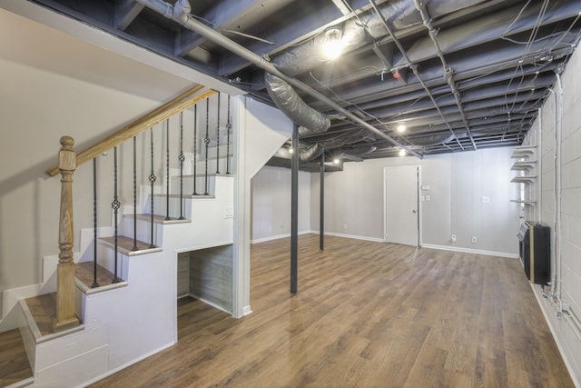 finished basement with stairs, baseboards, wood finished floors, and heating unit