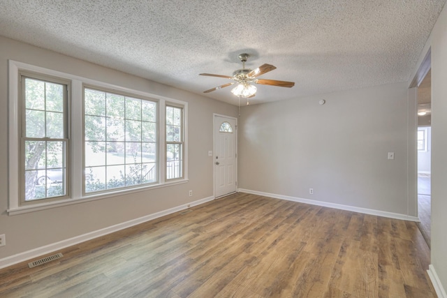 unfurnished room with visible vents, ceiling fan, a textured ceiling, wood finished floors, and baseboards