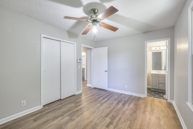 unfurnished bedroom with ensuite bath, a textured ceiling, ceiling fan, wood-type flooring, and a closet