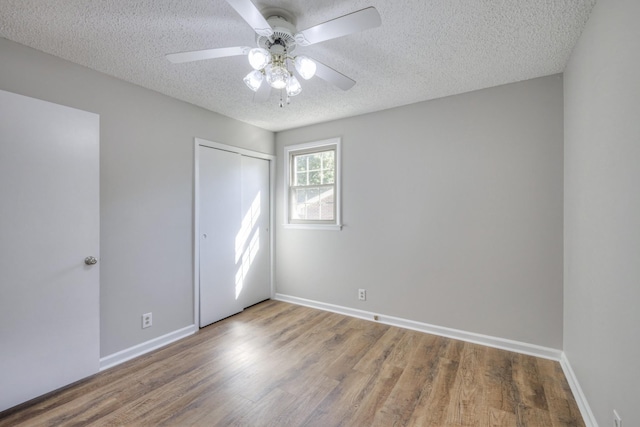 unfurnished bedroom with ceiling fan, a closet, wood-type flooring, and a textured ceiling