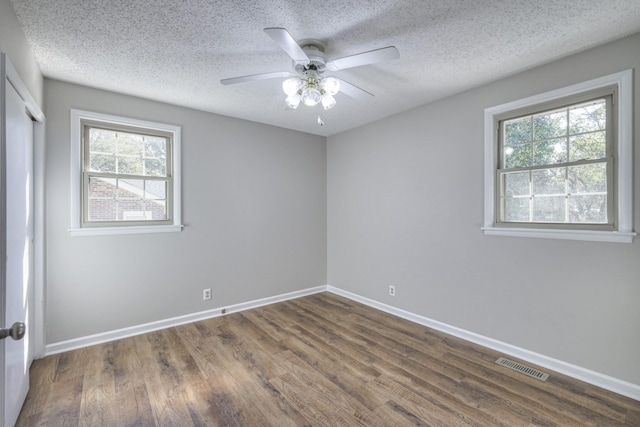 unfurnished room featuring ceiling fan, plenty of natural light, dark wood-type flooring, and a textured ceiling