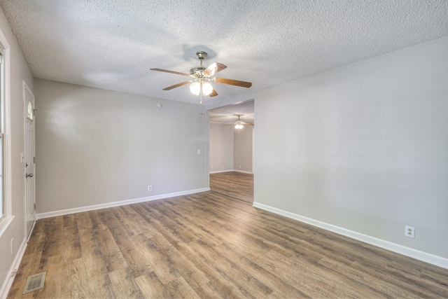 unfurnished room featuring a textured ceiling, ceiling fan, wood finished floors, visible vents, and baseboards