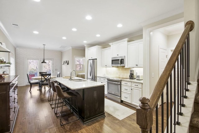 kitchen with a center island with sink, sink, hanging light fixtures, white cabinetry, and stainless steel appliances