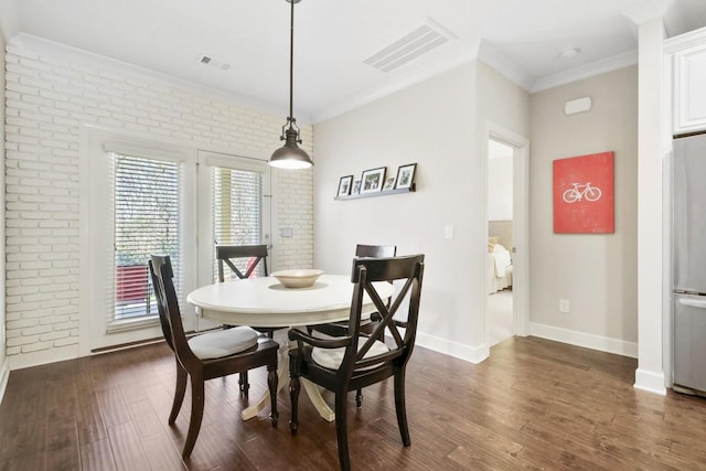 dining space featuring dark hardwood / wood-style floors, ornamental molding, and brick wall