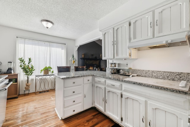 kitchen featuring white cabinetry, light stone counters, kitchen peninsula, wood-type flooring, and white electric stovetop