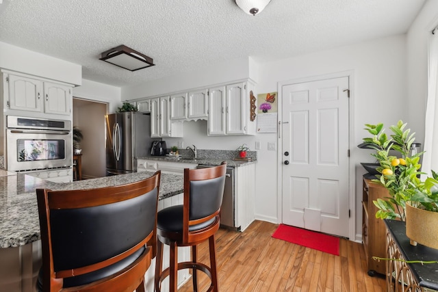 kitchen with stainless steel refrigerator, sink, light hardwood / wood-style floors, a textured ceiling, and white cabinets