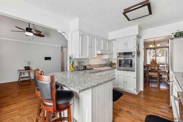 kitchen with white cabinetry, kitchen peninsula, a breakfast bar, ceiling fan with notable chandelier, and appliances with stainless steel finishes