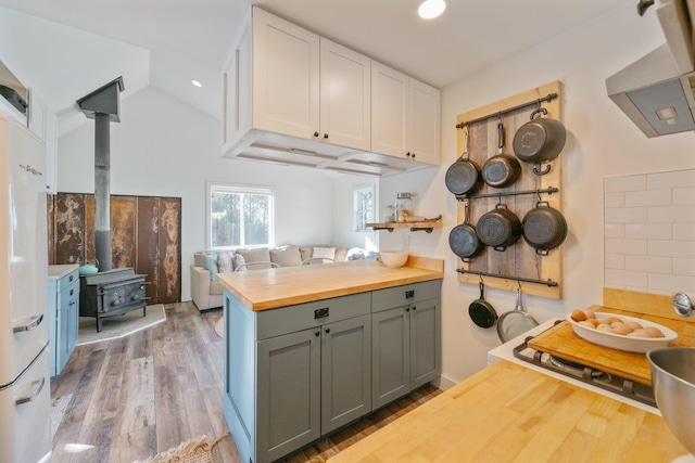 kitchen with lofted ceiling, a wood stove, wooden counters, white cabinets, and light hardwood / wood-style flooring