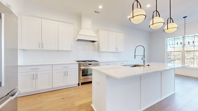 kitchen featuring white cabinetry, stainless steel appliances, an island with sink, pendant lighting, and custom range hood