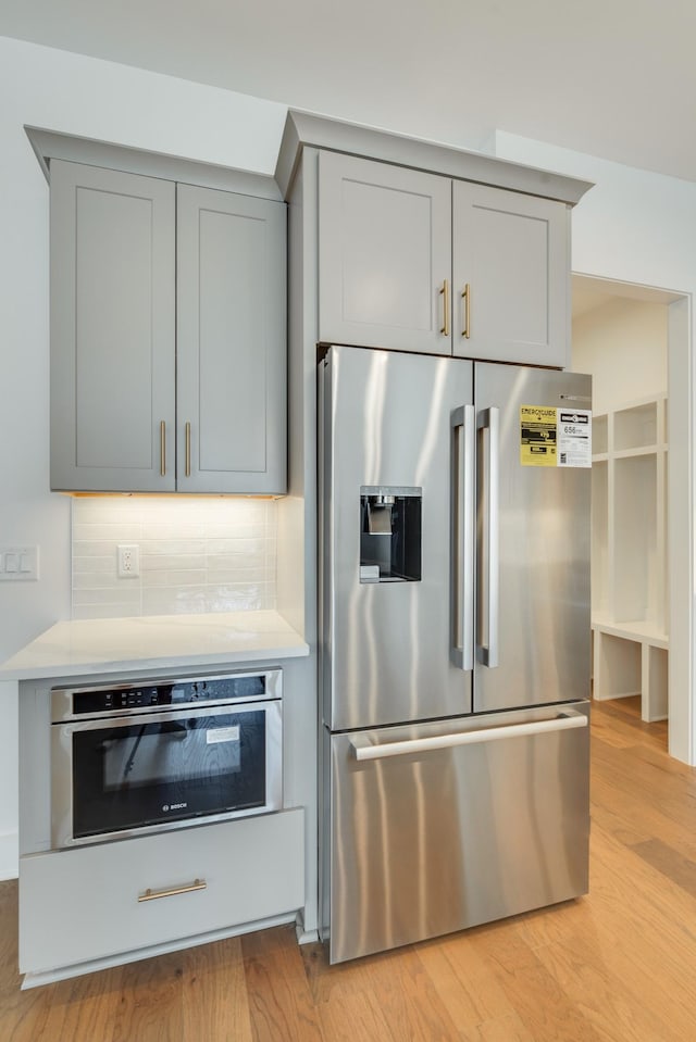 kitchen with gray cabinets, decorative backsplash, light wood-type flooring, and appliances with stainless steel finishes