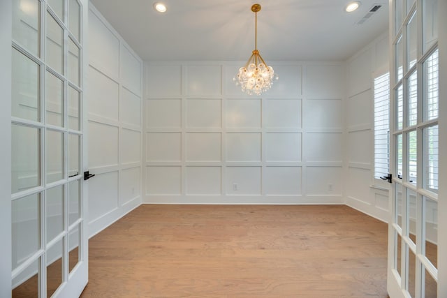 unfurnished room with french doors, light hardwood / wood-style floors, and an inviting chandelier