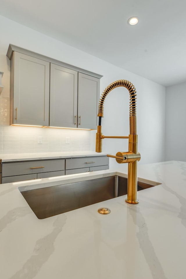 interior details featuring gray cabinetry, decorative backsplash, light stone counters, and sink