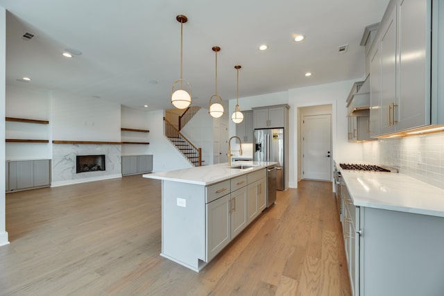 kitchen with sink, a high end fireplace, decorative light fixtures, gray cabinets, and a kitchen island with sink