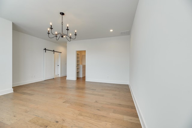 unfurnished room with a barn door, light hardwood / wood-style floors, and an inviting chandelier