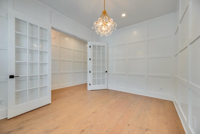 spare room featuring french doors, hardwood / wood-style flooring, built in features, and a notable chandelier